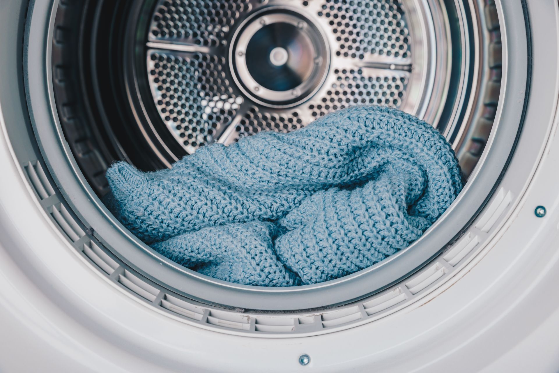 View of a cozy blue knitted blanket inside a modern washing machine drum. View of a cozy blue knitted blanket inside a modern washing machine drum.