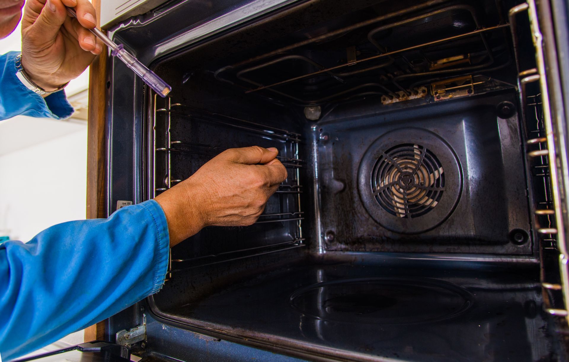 Person inspecting an oven interior, using a tool. The oven is black inside.