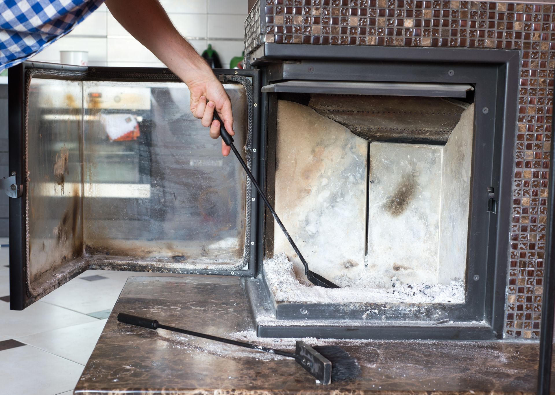 Person cleaning a fireplace with a long-handled tool; ash inside and on the hearth.