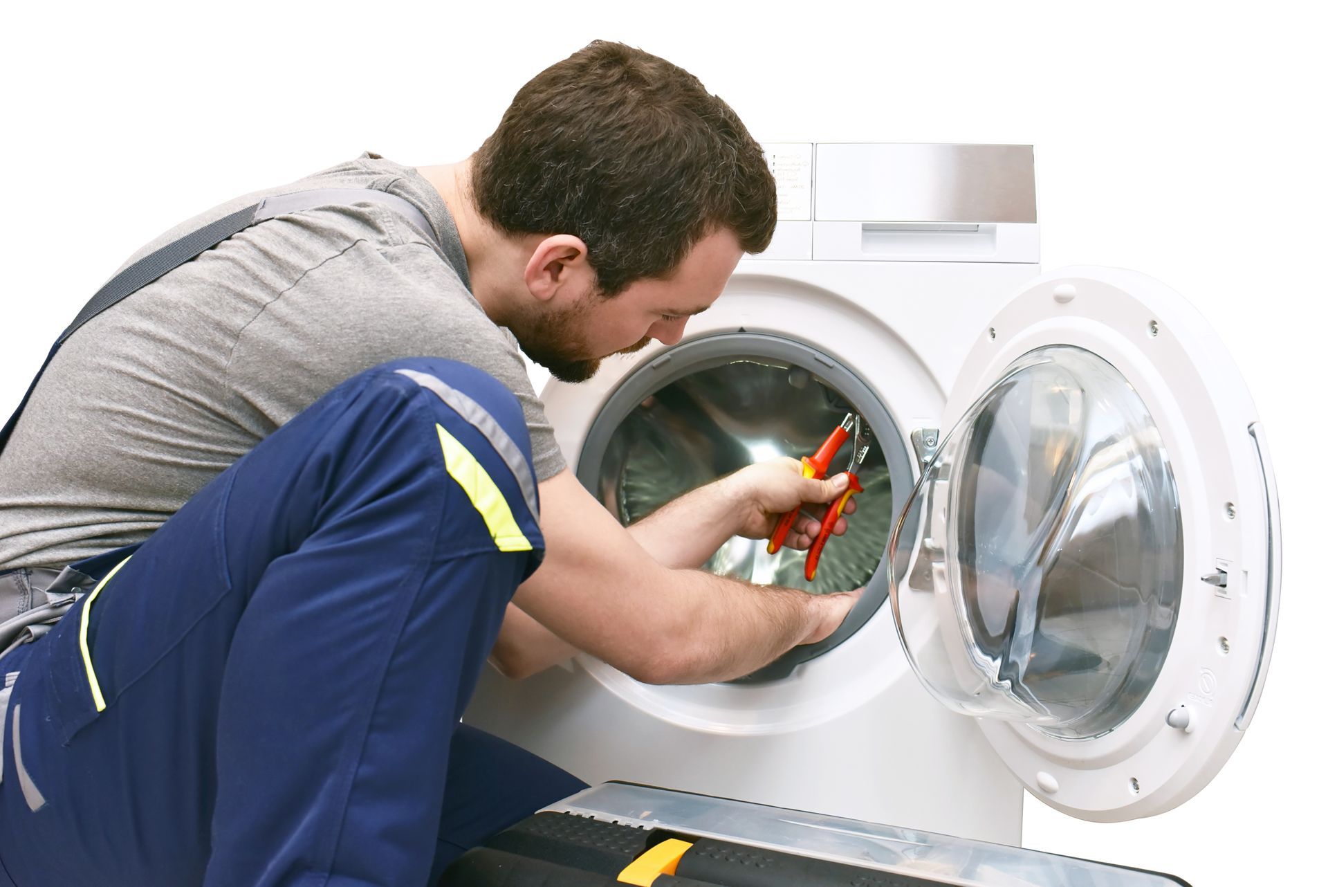 A person repairs a washing machine, using pliers. They kneel near open door.