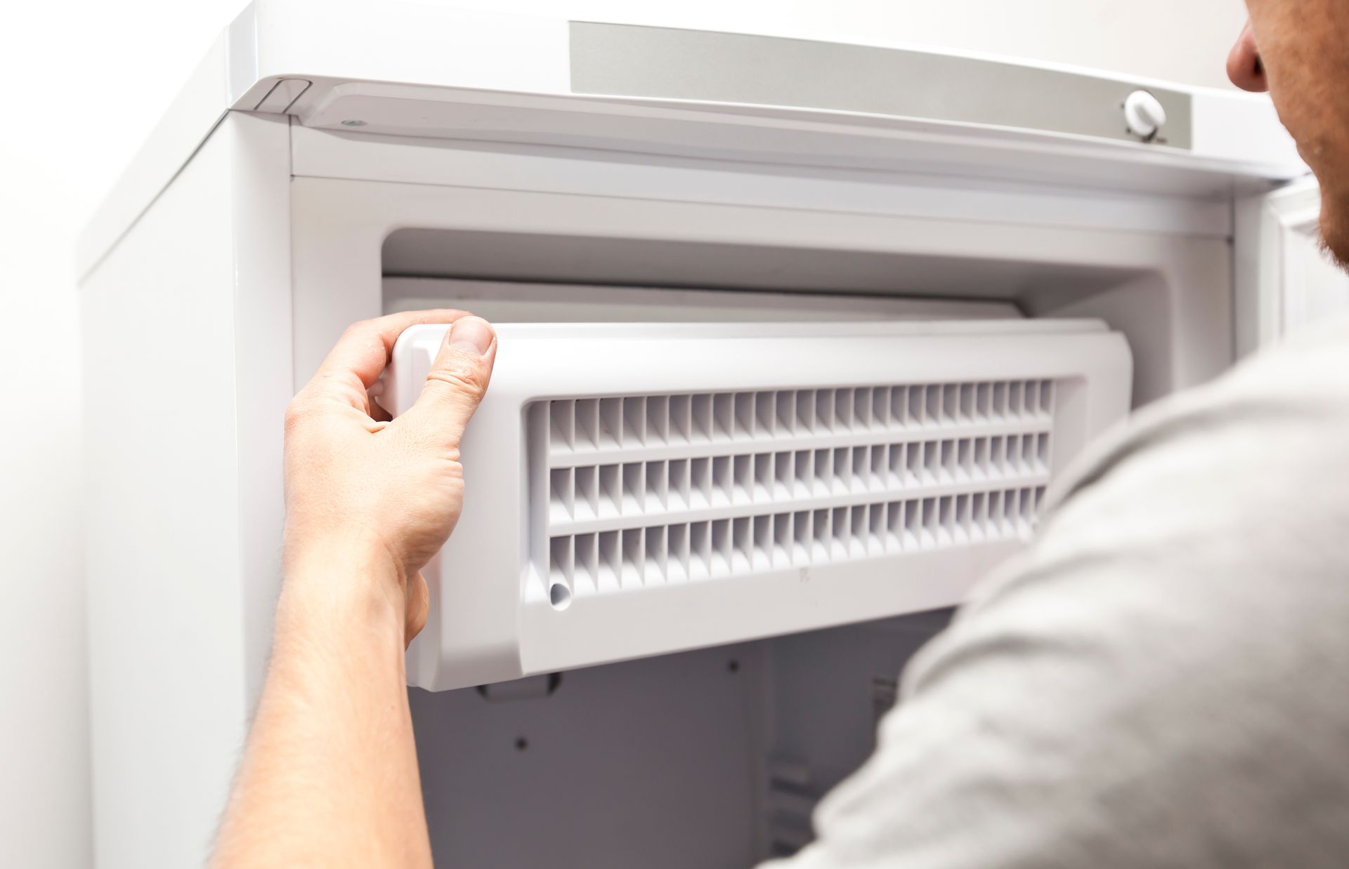 Man removing a white refrigerator component with a grid-like pattern.