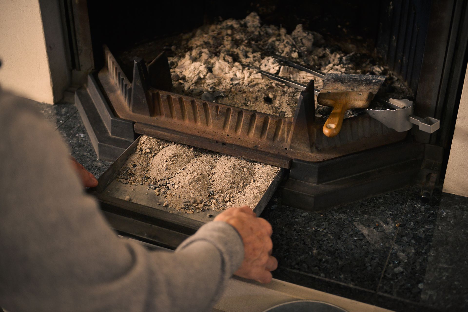 Person emptying ash tray from a fireplace, holding tray of gray ash.