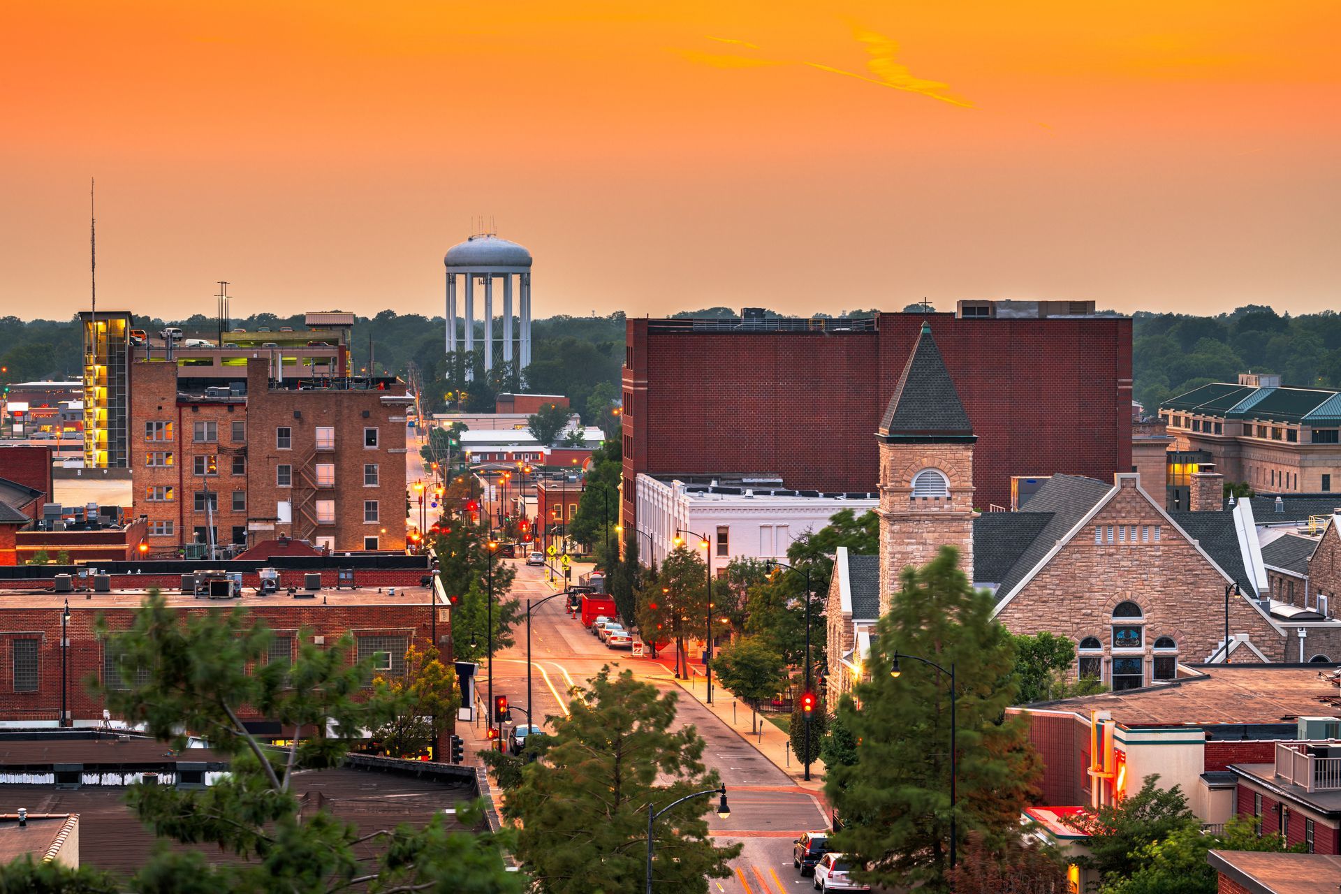 City skyline at sunset with a water tower, buildings, and street lit up.