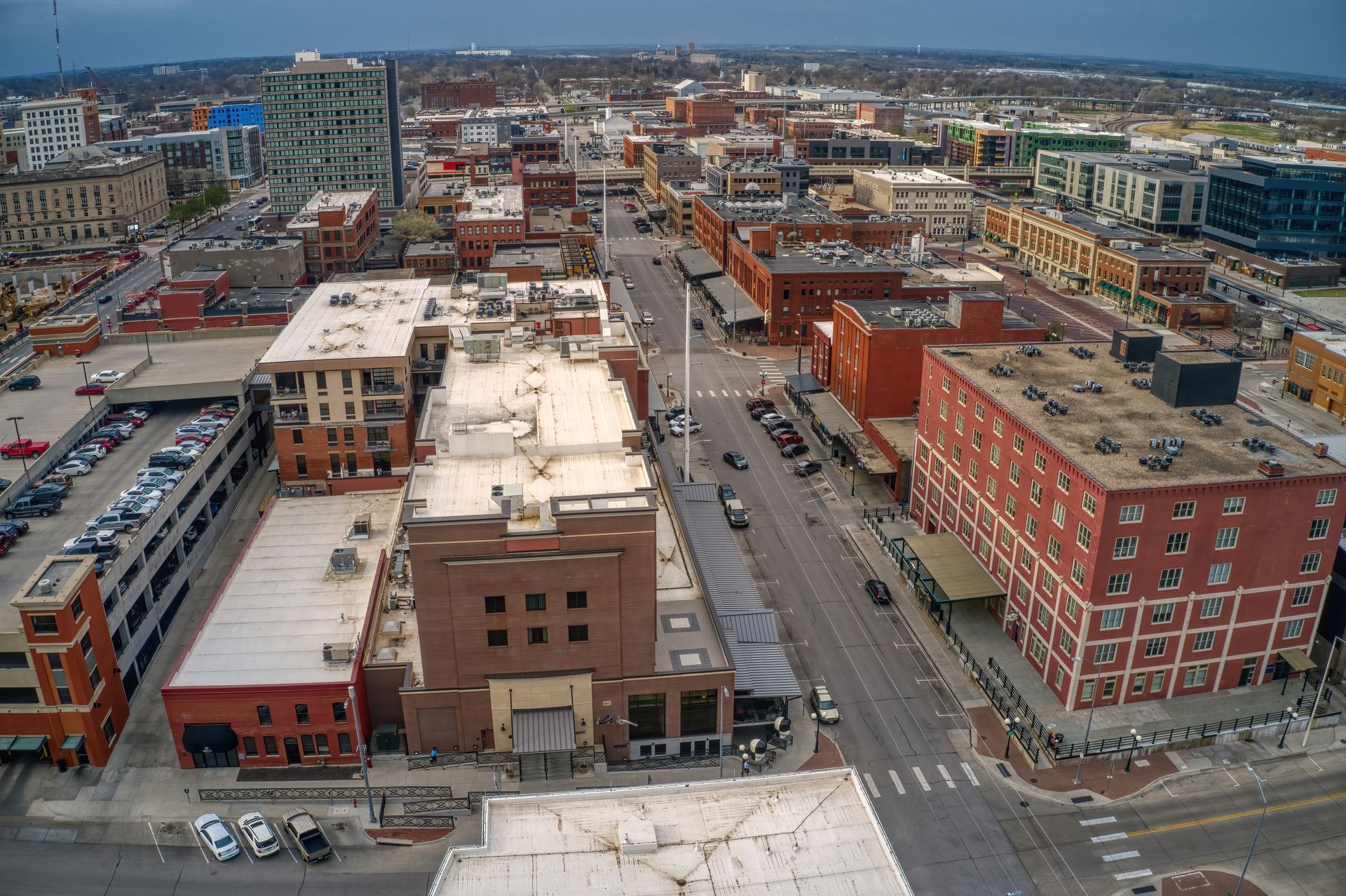 Aerial view of a city street with red brick buildings, cars, and a blue-green skyscraper in the background.