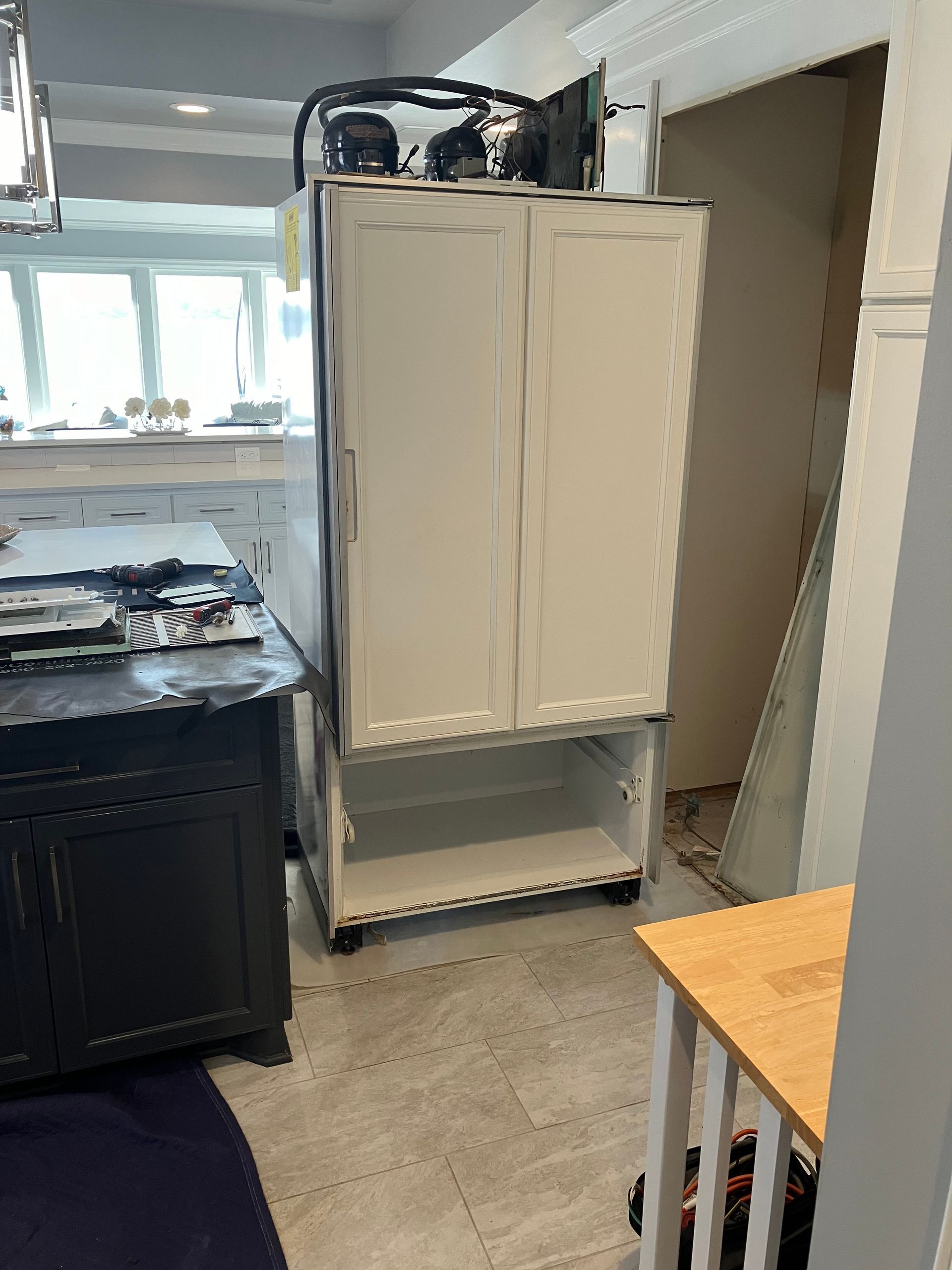 White cabinet on wheels in a kitchen; lower open shelf, air compressor on top.