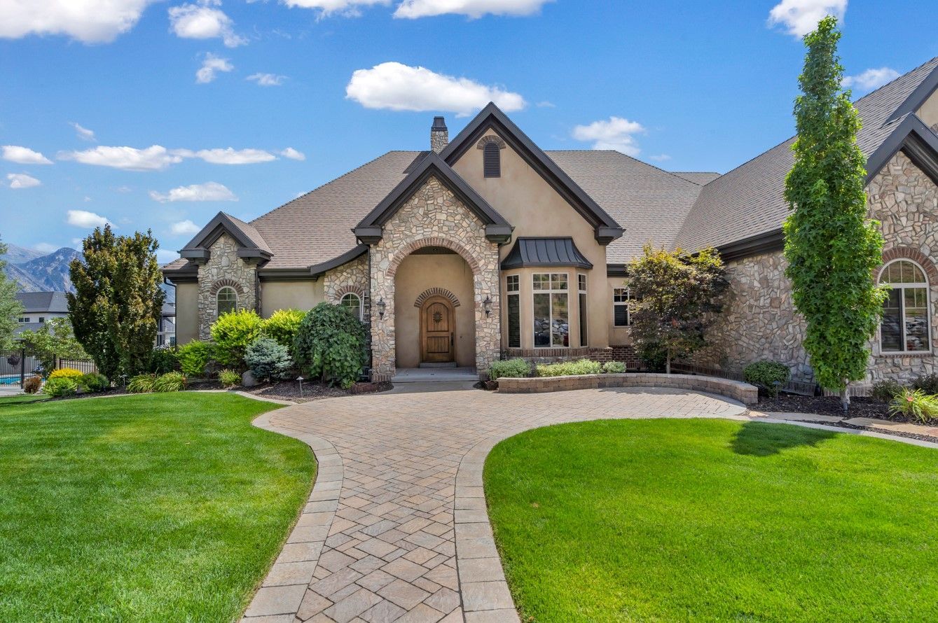 A large house with a lush green lawn and a brick driveway leading to it.