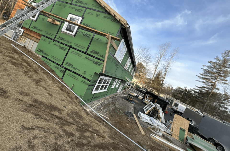 A house is being built with green siding and a ladder.