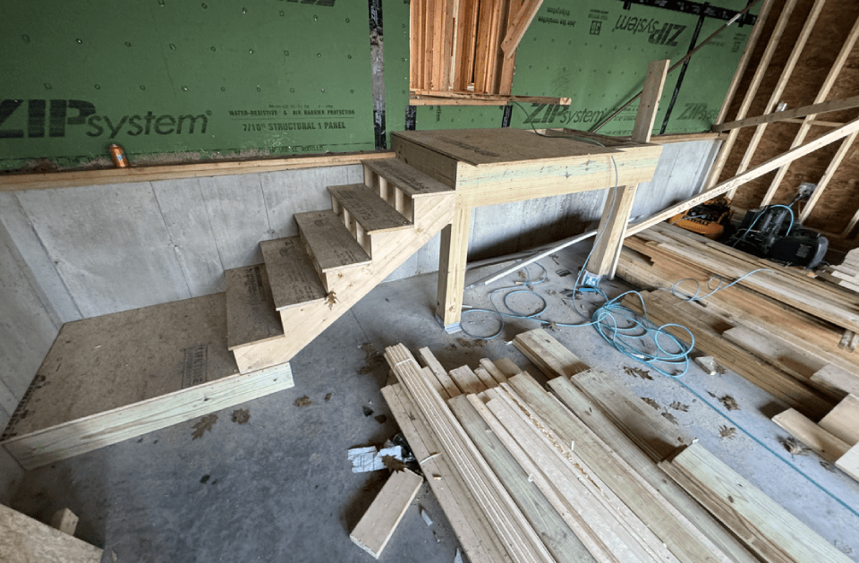 A wooden staircase is being built in a building under construction.