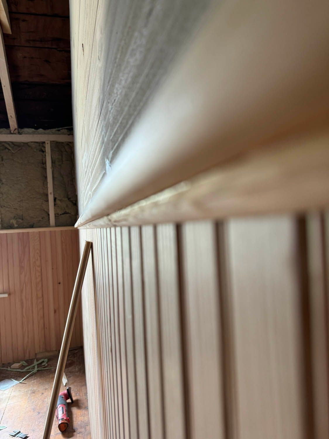 A close up of a wooden wall with a broom in the background.