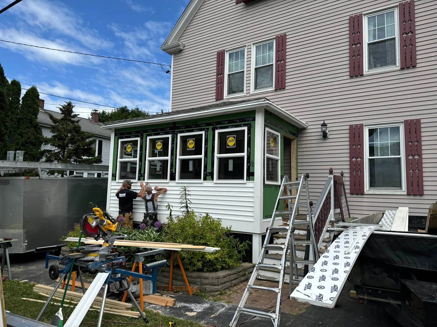 A group of people are working on a porch in front of a house.