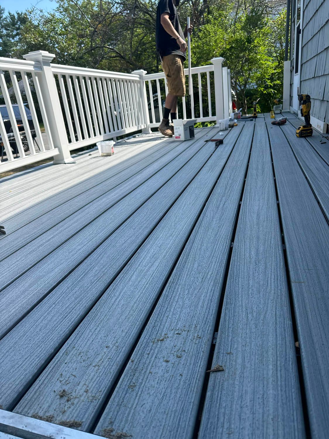 A man is standing on a wooden deck with a white railing.