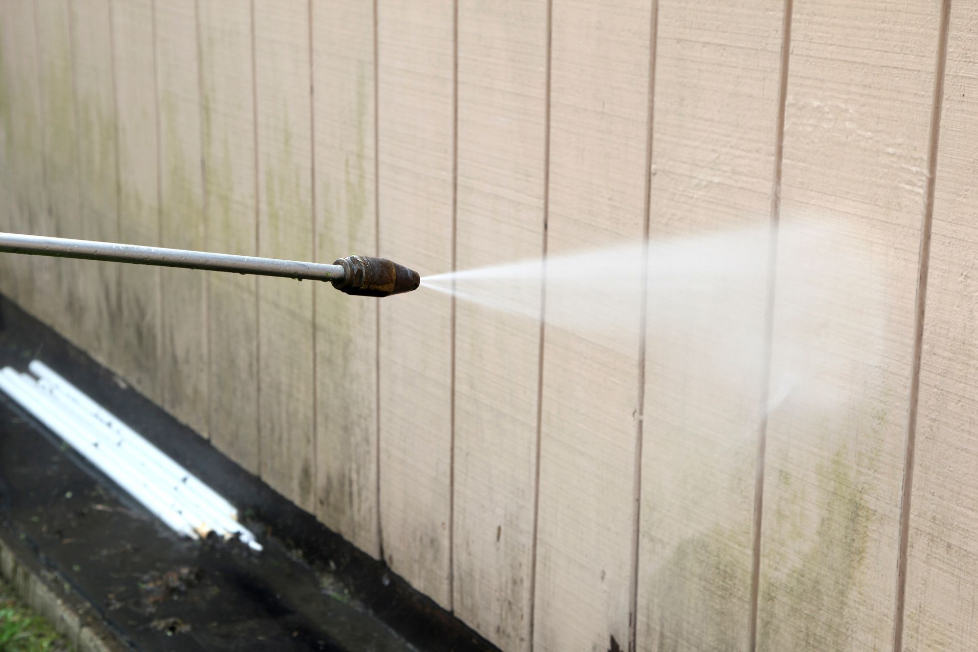 Pressure washing service in action cleaning exterior wall up close with machine.