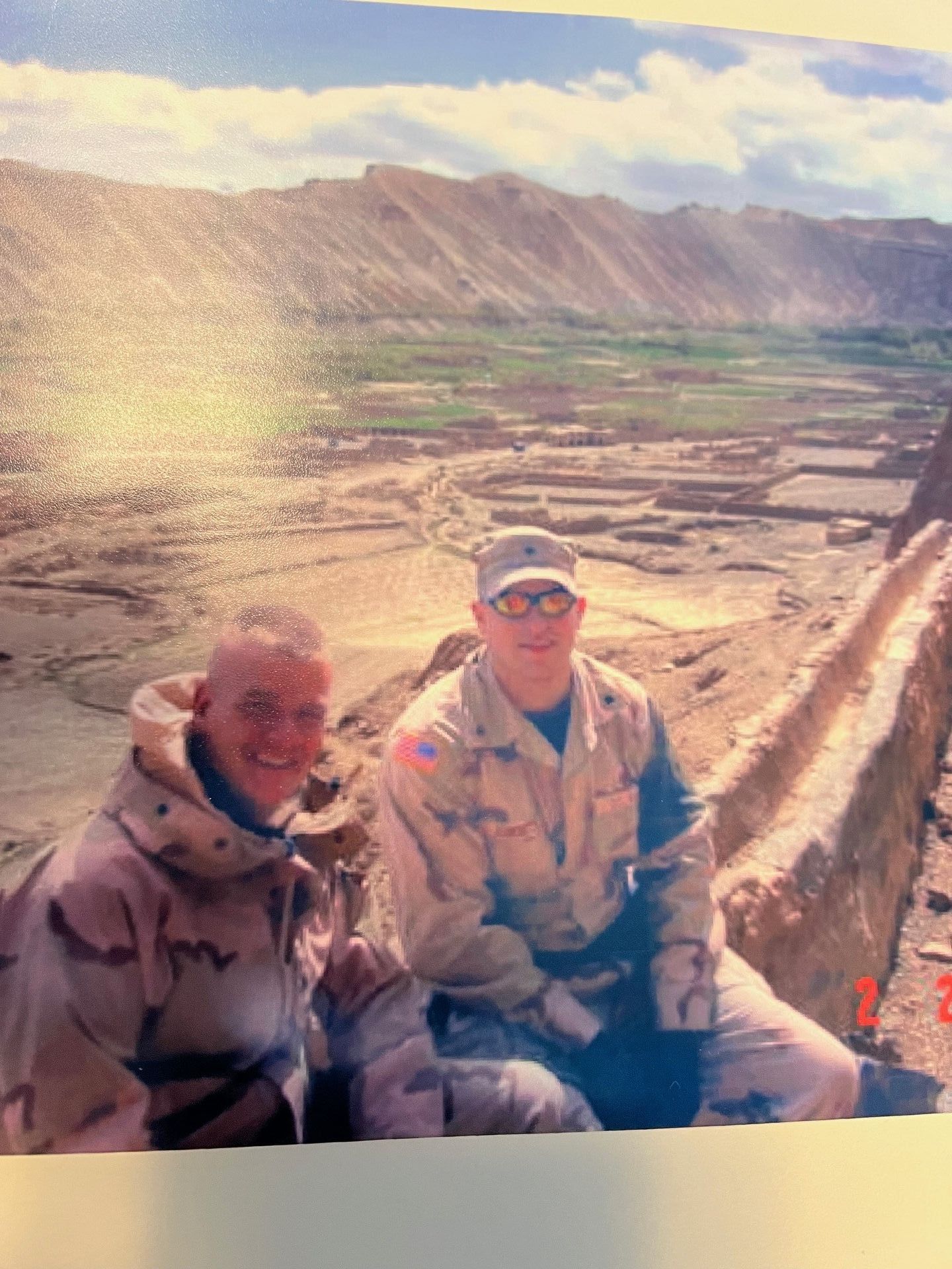 Two men in military uniforms are sitting next to each other in front of a mountain.