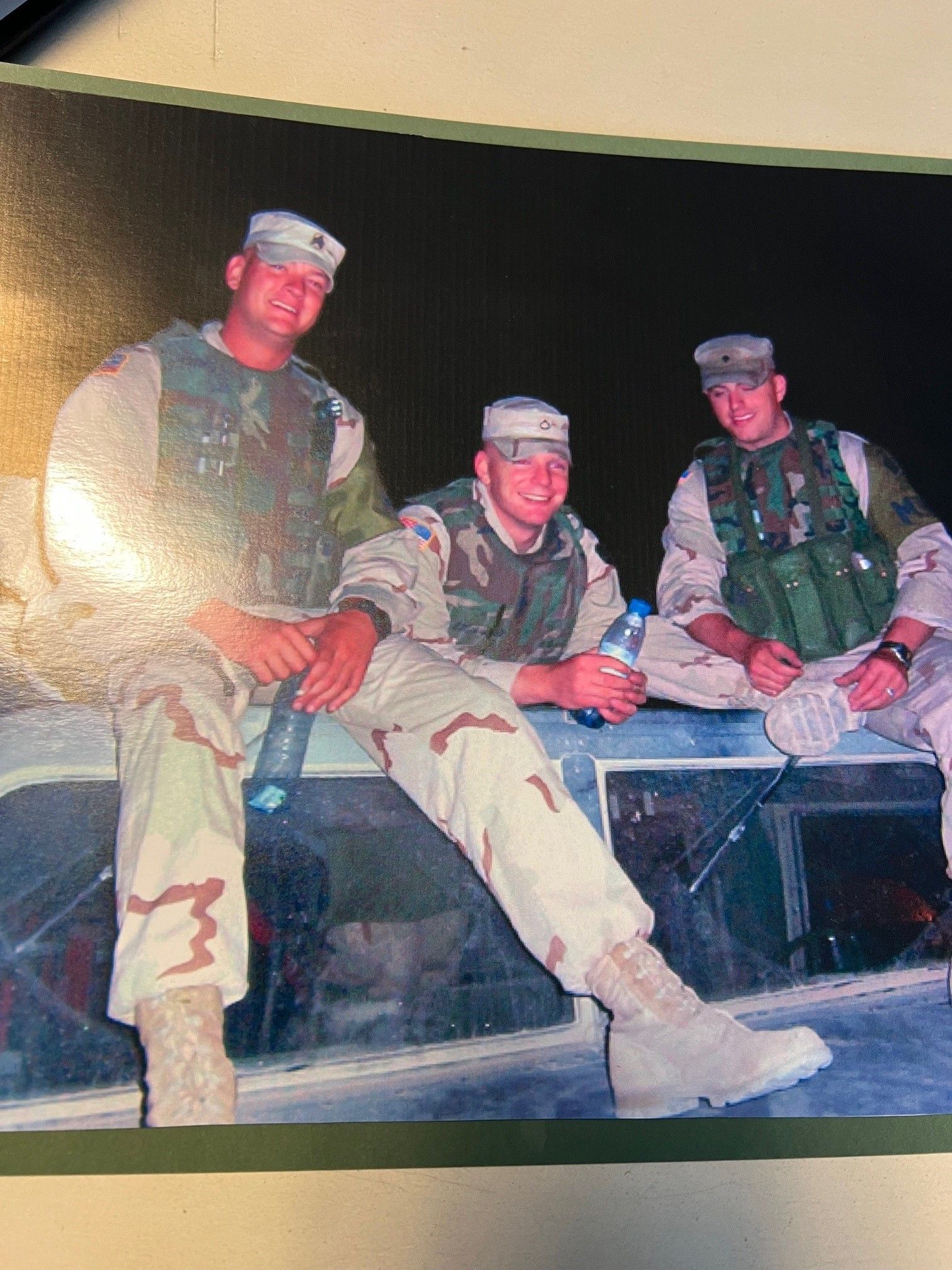Three soldiers are sitting on the hood of a truck