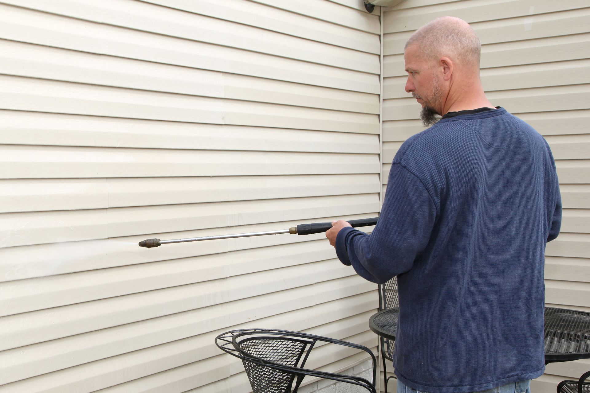 Man with high-pressure washing machine cleaning wall, professional pressure washing service.