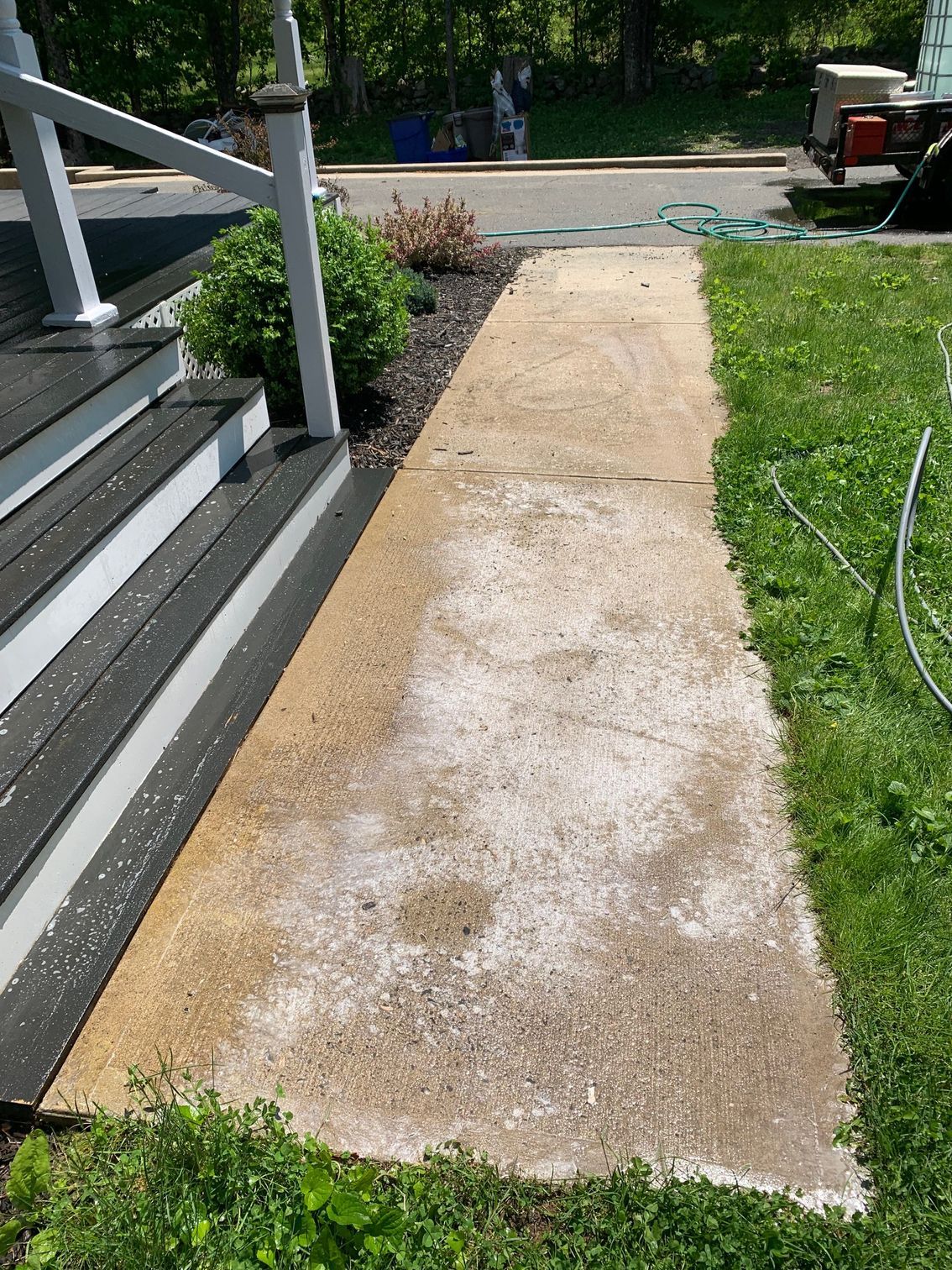 A concrete walkway next to a house with stairs and grass.