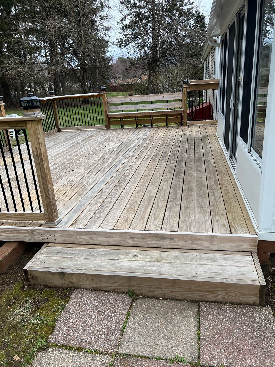 Wooden deck with steps, a built-in bench, and a railing, next to a house with windows.