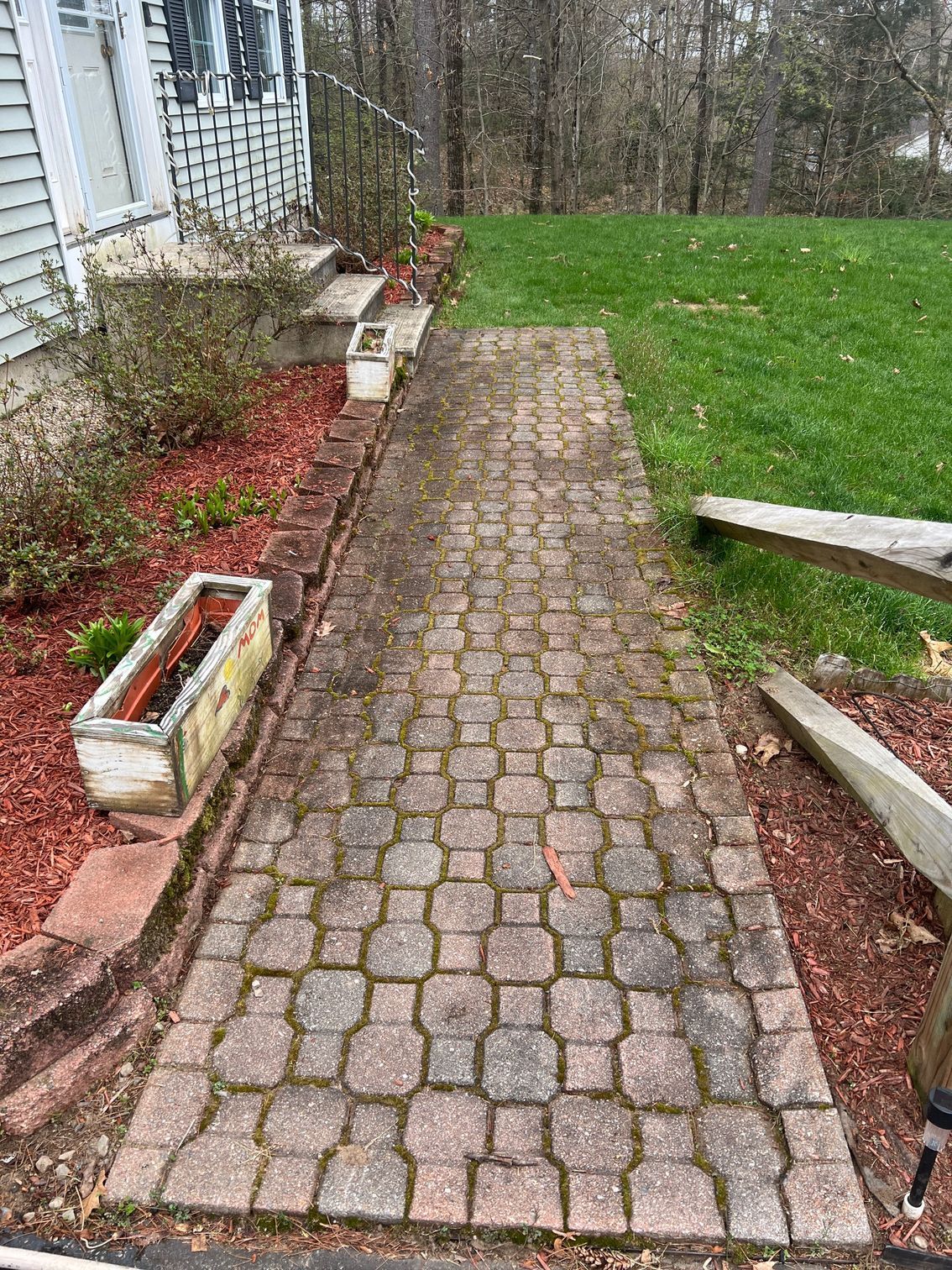 A brick walkway leading to a house in a backyard.