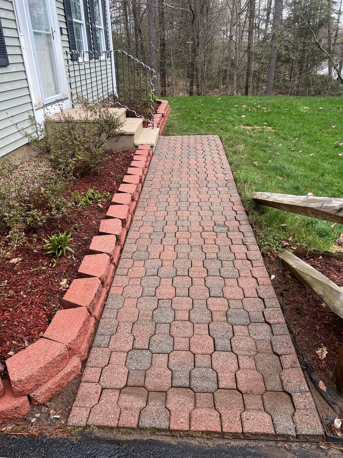 A brick walkway leading to a house next to a lush green yard.