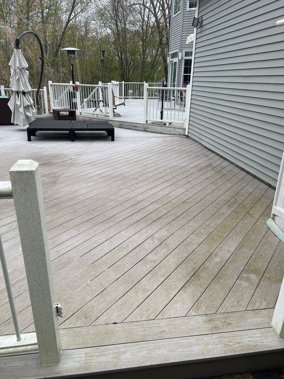 Wooden deck, faded and weathered, extends from the side of a gray house, with a railing.