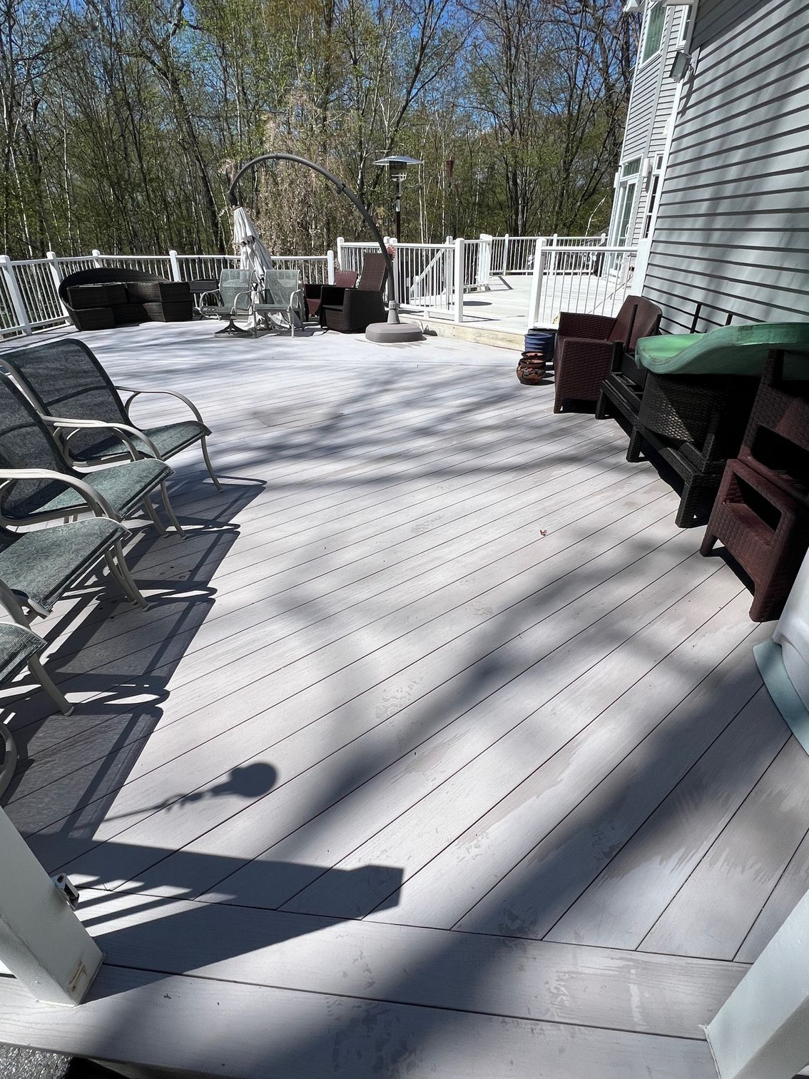 Gray wooden deck with various chairs and furniture, surrounded by a white railing and trees in the background.