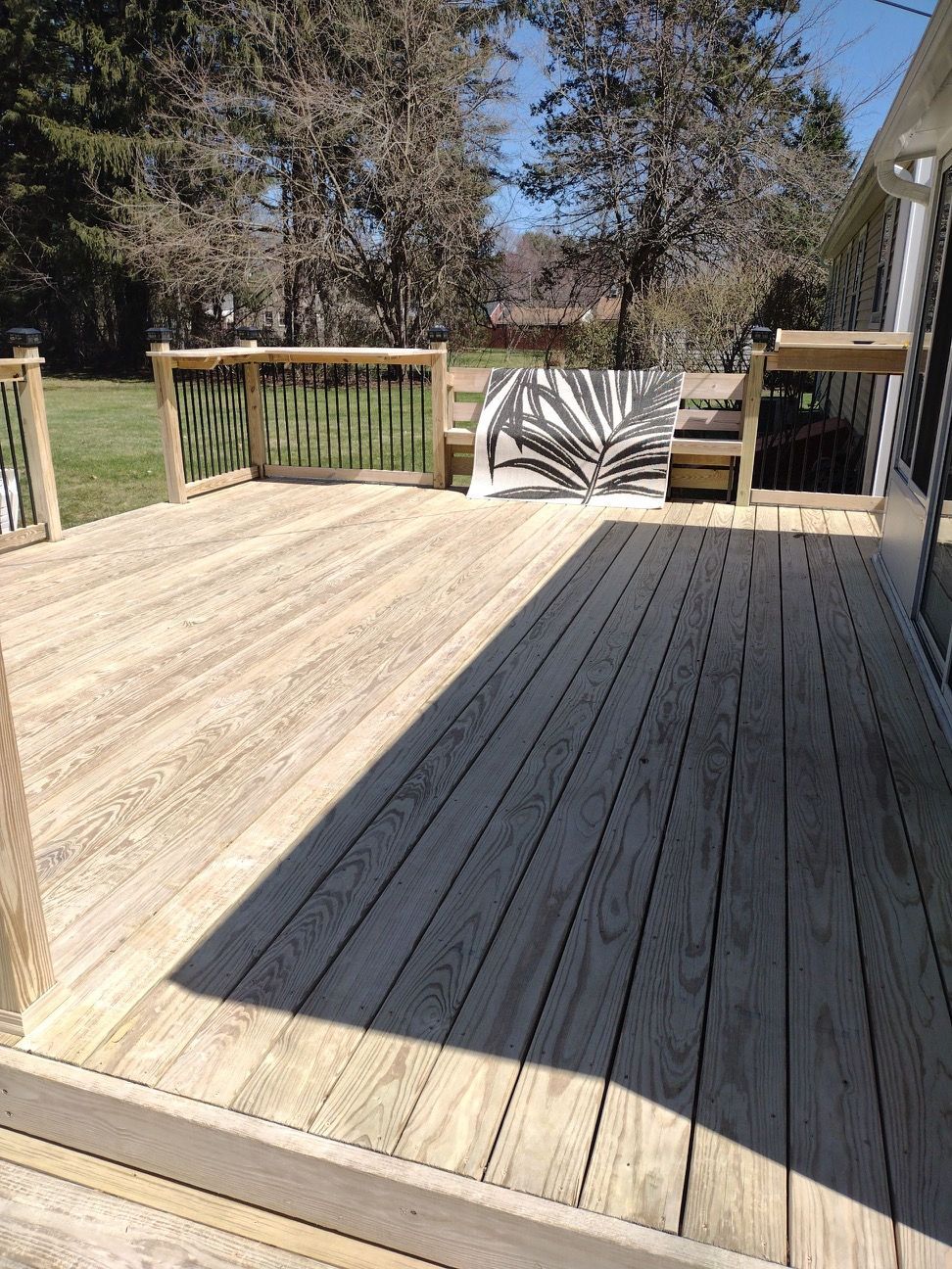 Wooden deck in sunlight, with a fence and a leaf design on the wall.