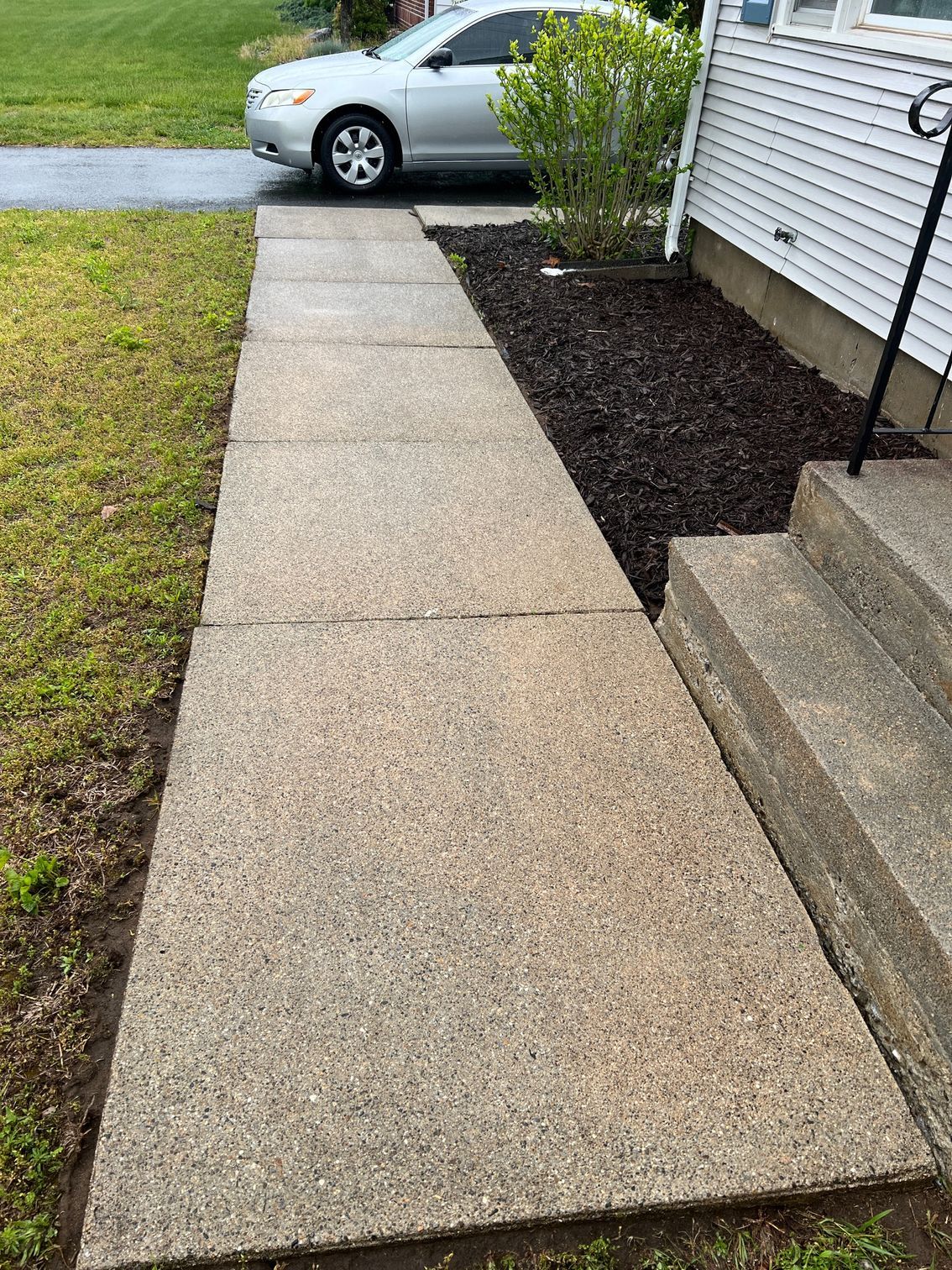 A car is parked on the side of a sidewalk next to a house.