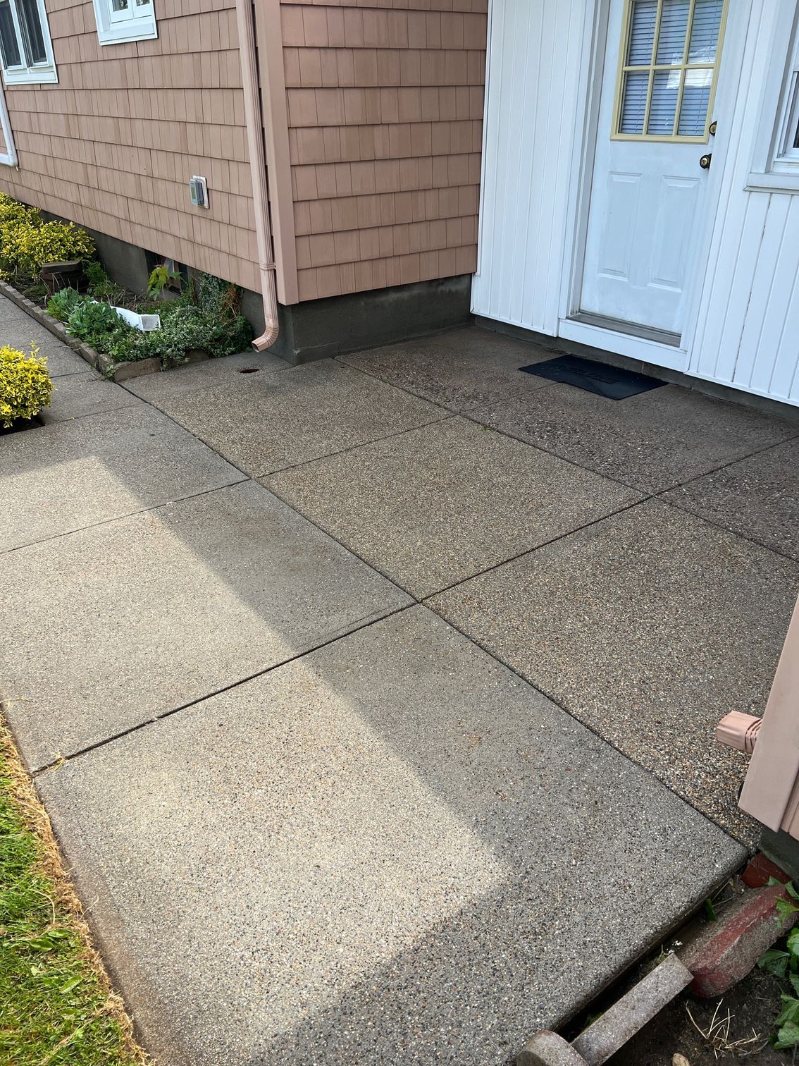 Cement walkway leading to a white door. The walkway is bordered by grass and building exterior.