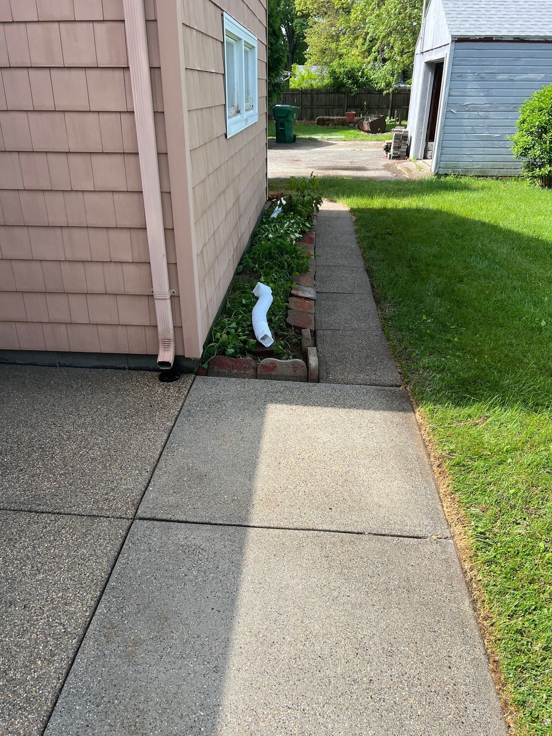A sidewalk leading to a house with a garden in the backyard.