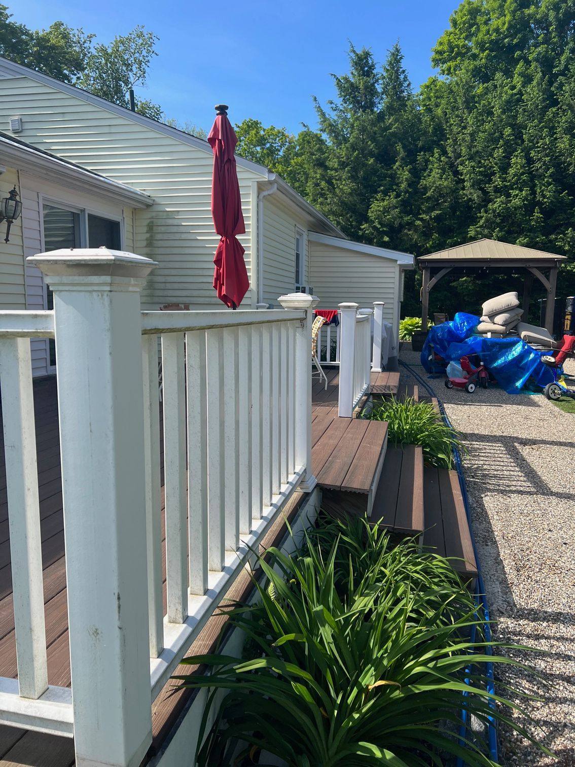 Deck with white railing, red umbrella, and flowerbed.  Gazebo and yard beyond.