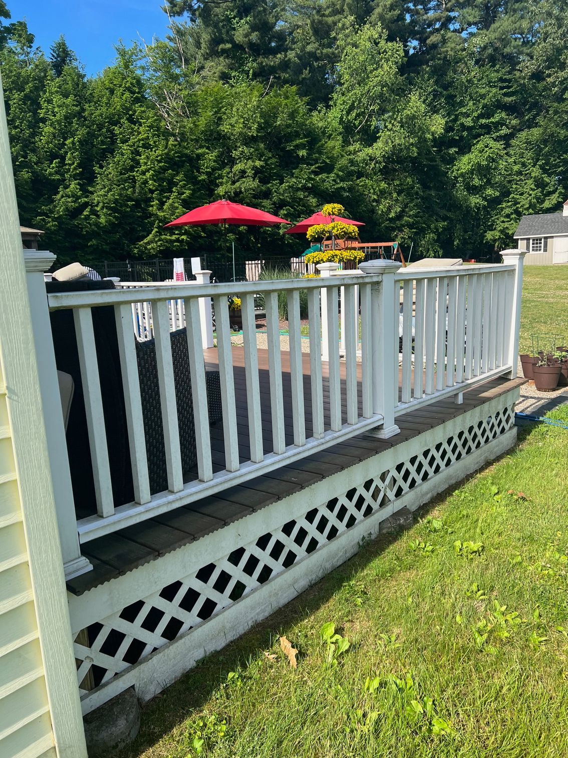 White deck with lattice, overlooking a green lawn with trees and red umbrellas.