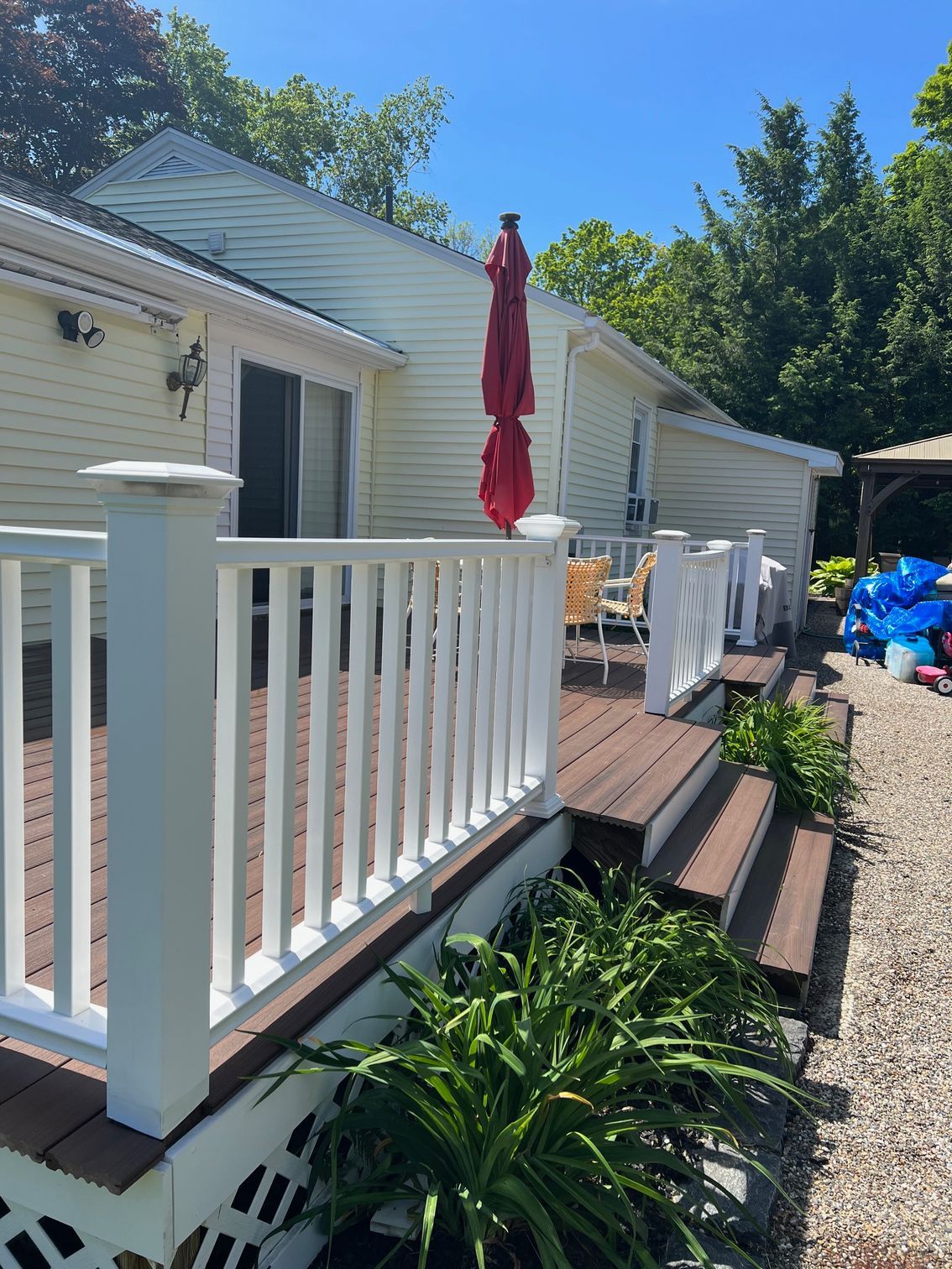 Deck with white railing, brown steps, and a red umbrella in front of a light yellow house.
