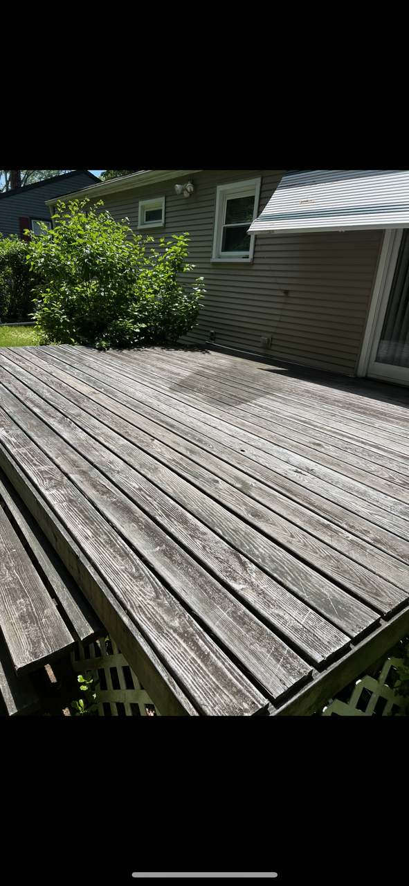 Wooden deck with weathered planks next to a house with shrubs.
