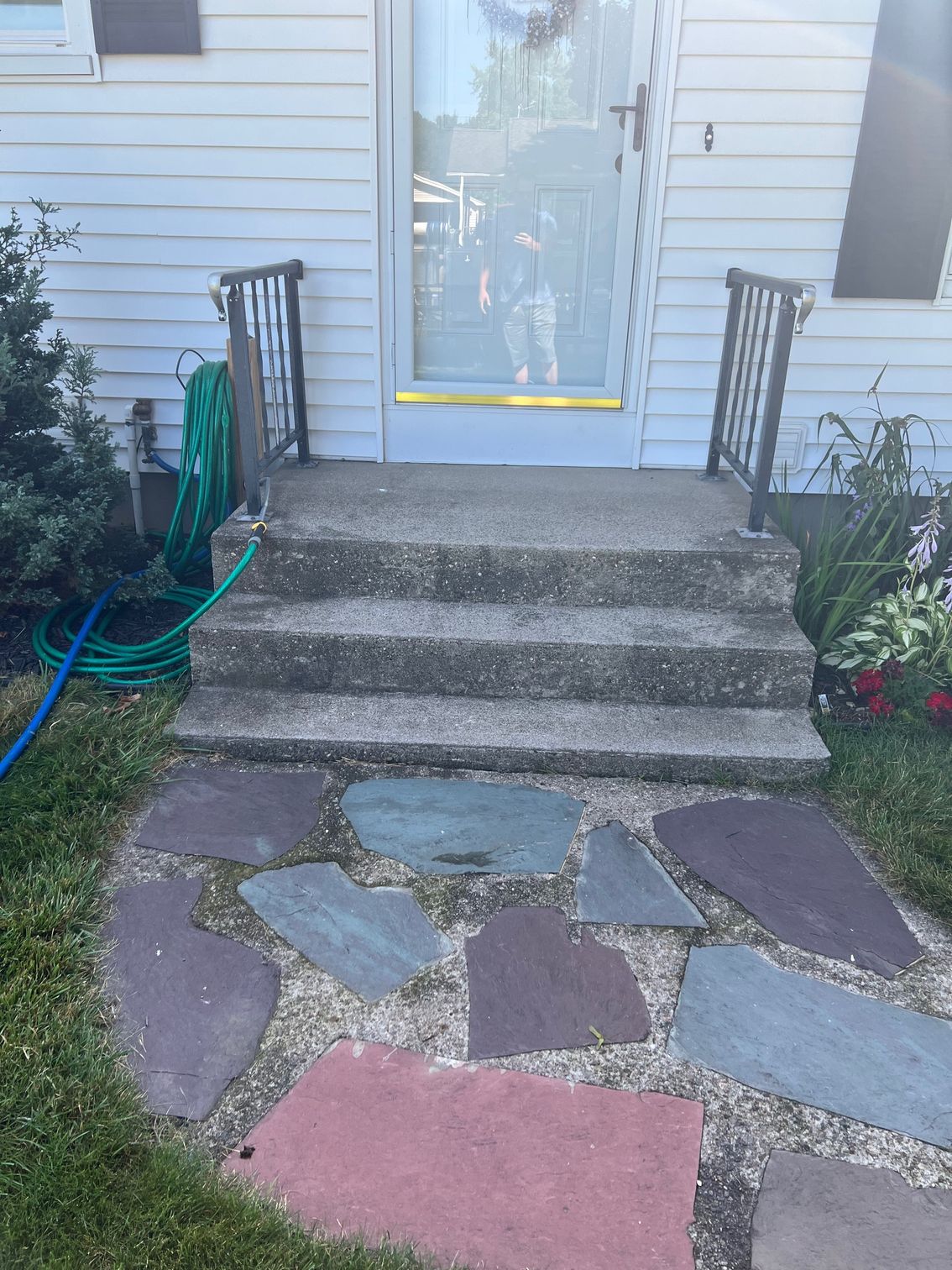 Concrete steps lead to a front door with handrails. A stone pathway winds through a grassy yard.