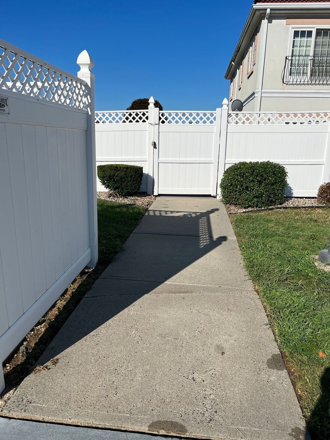 A concrete walkway leading to a white fence and gate