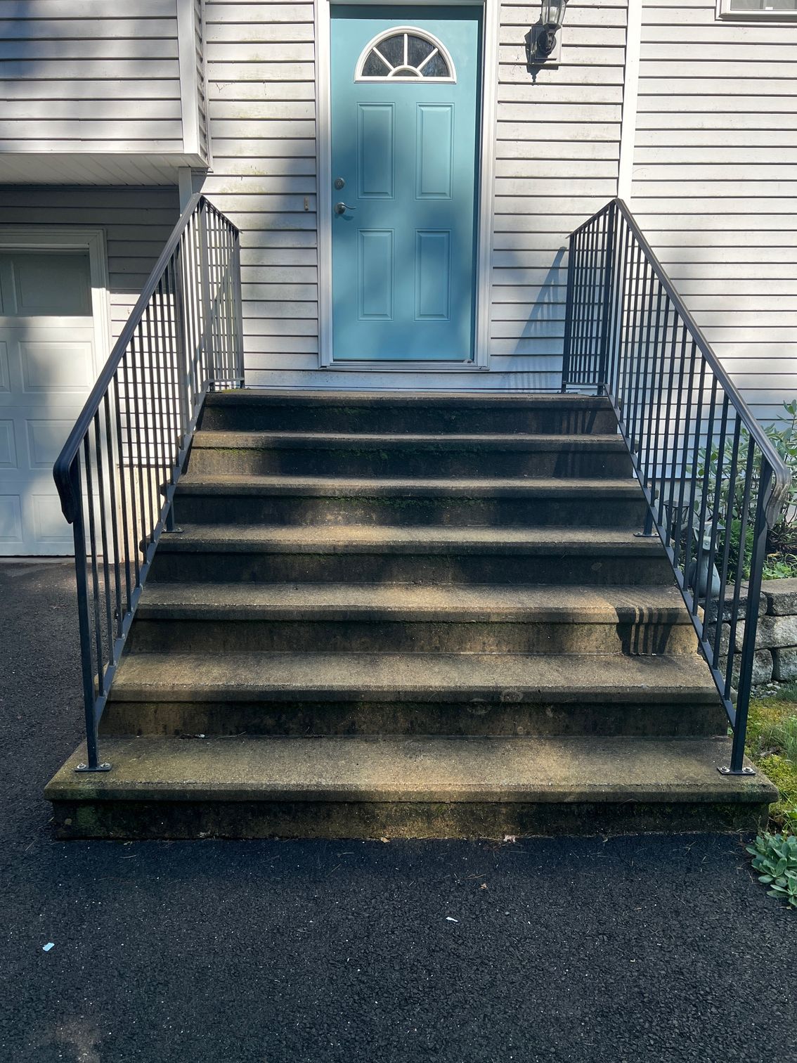 Concrete steps leading up to a blue front door, with black metal railings on either side.