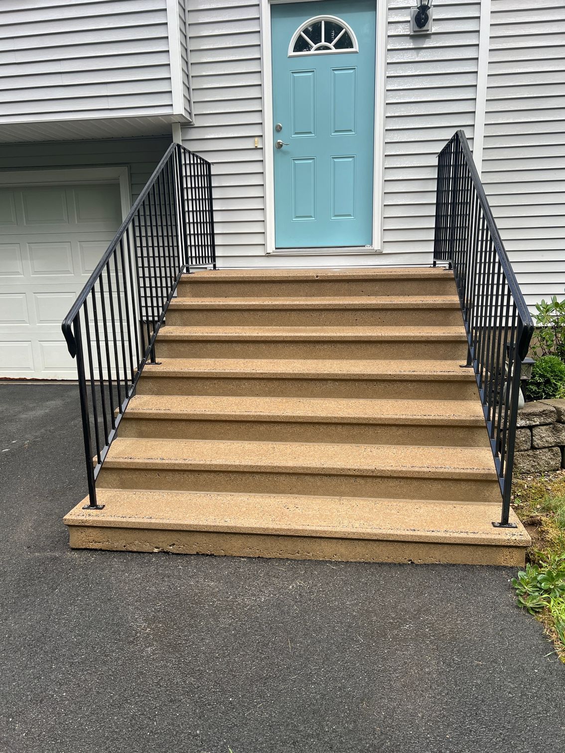 Exterior shot of steps leading to a blue door, black railing on each side.