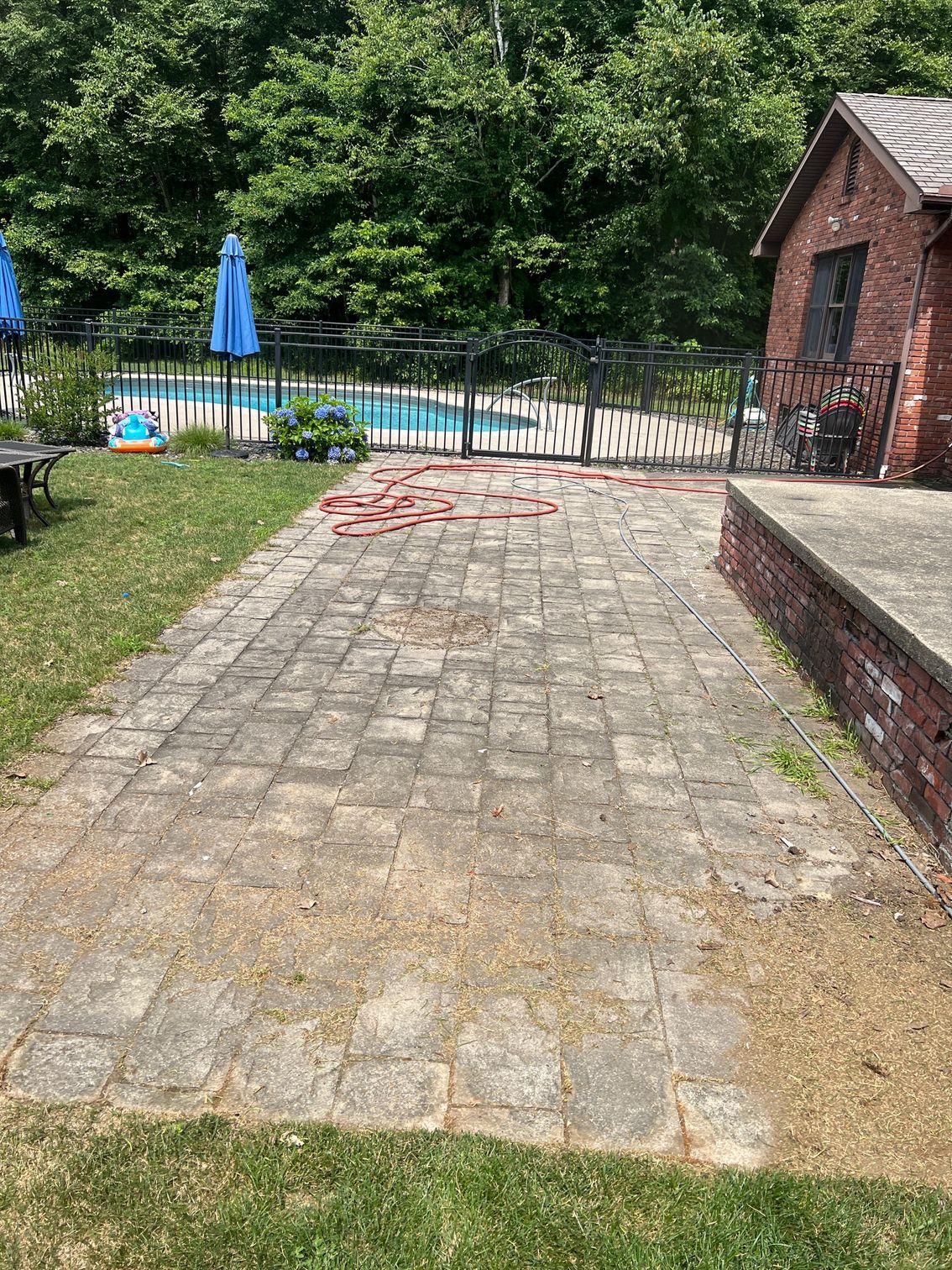 Brick patio next to a pool and building. Red bricks scattered across. Green grass surrounds.