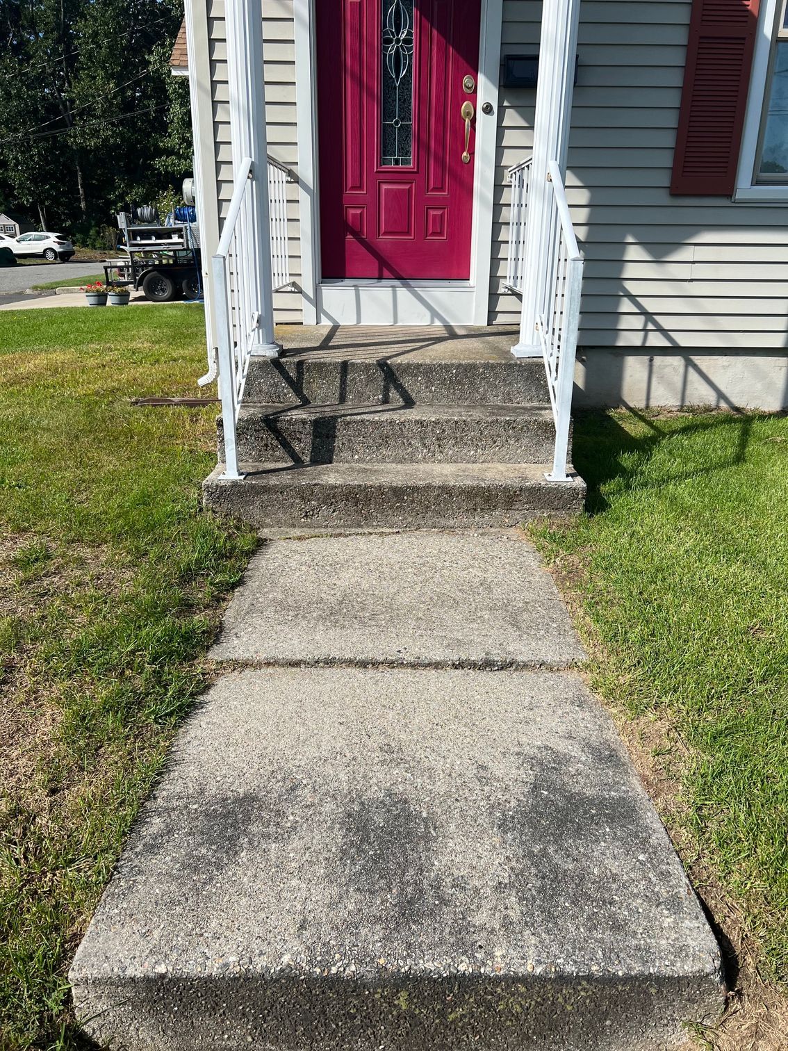 A concrete walkway leading to a red door of a house.
