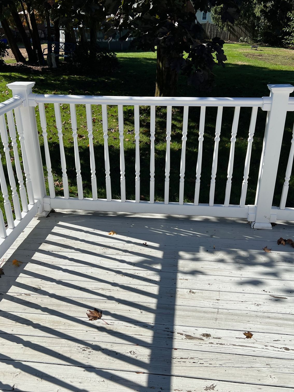 White deck railing casting shadows on weathered deck boards; green lawn in background.
