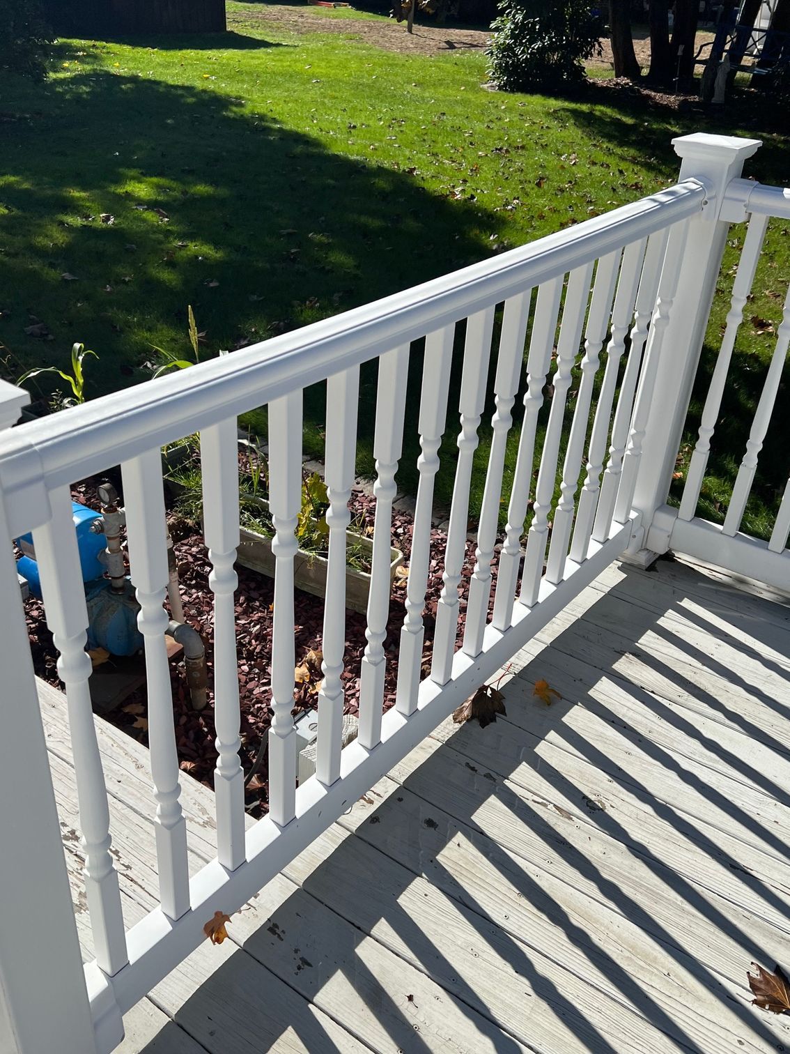 White deck railing on a sunny day. Green grass and trees are in the background.