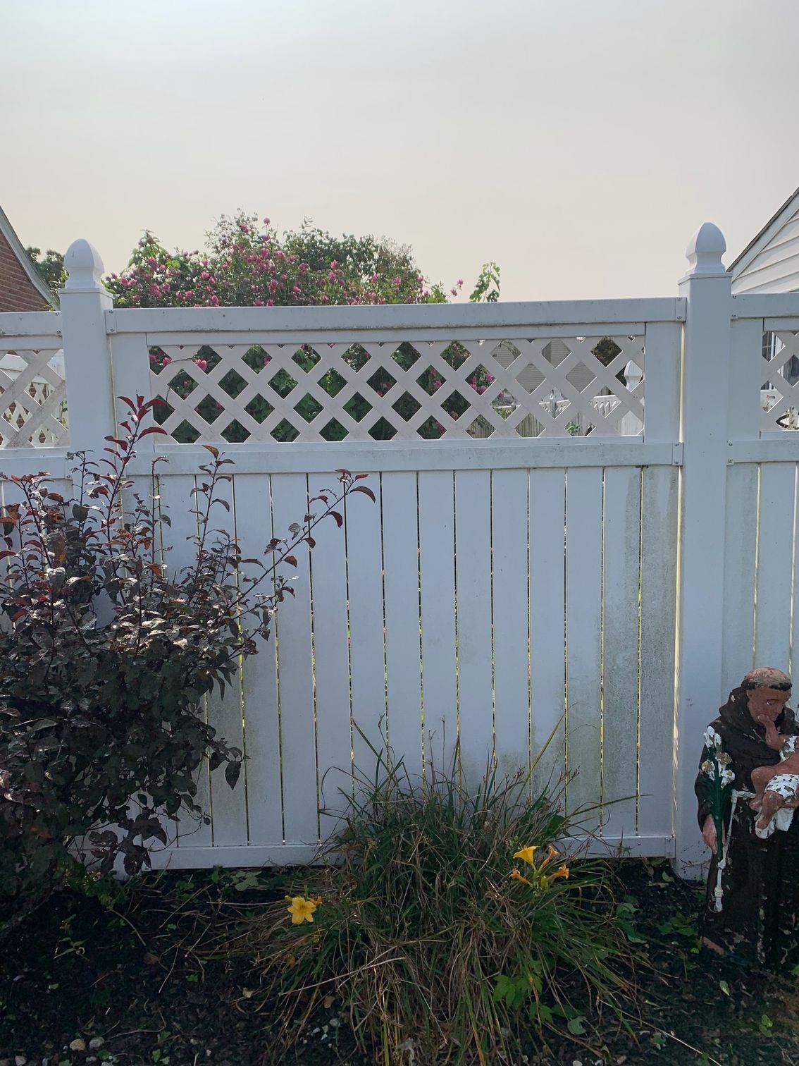 White wooden fence with lattice top, separating a yard from an unseen area, with foliage and a figure on one side.