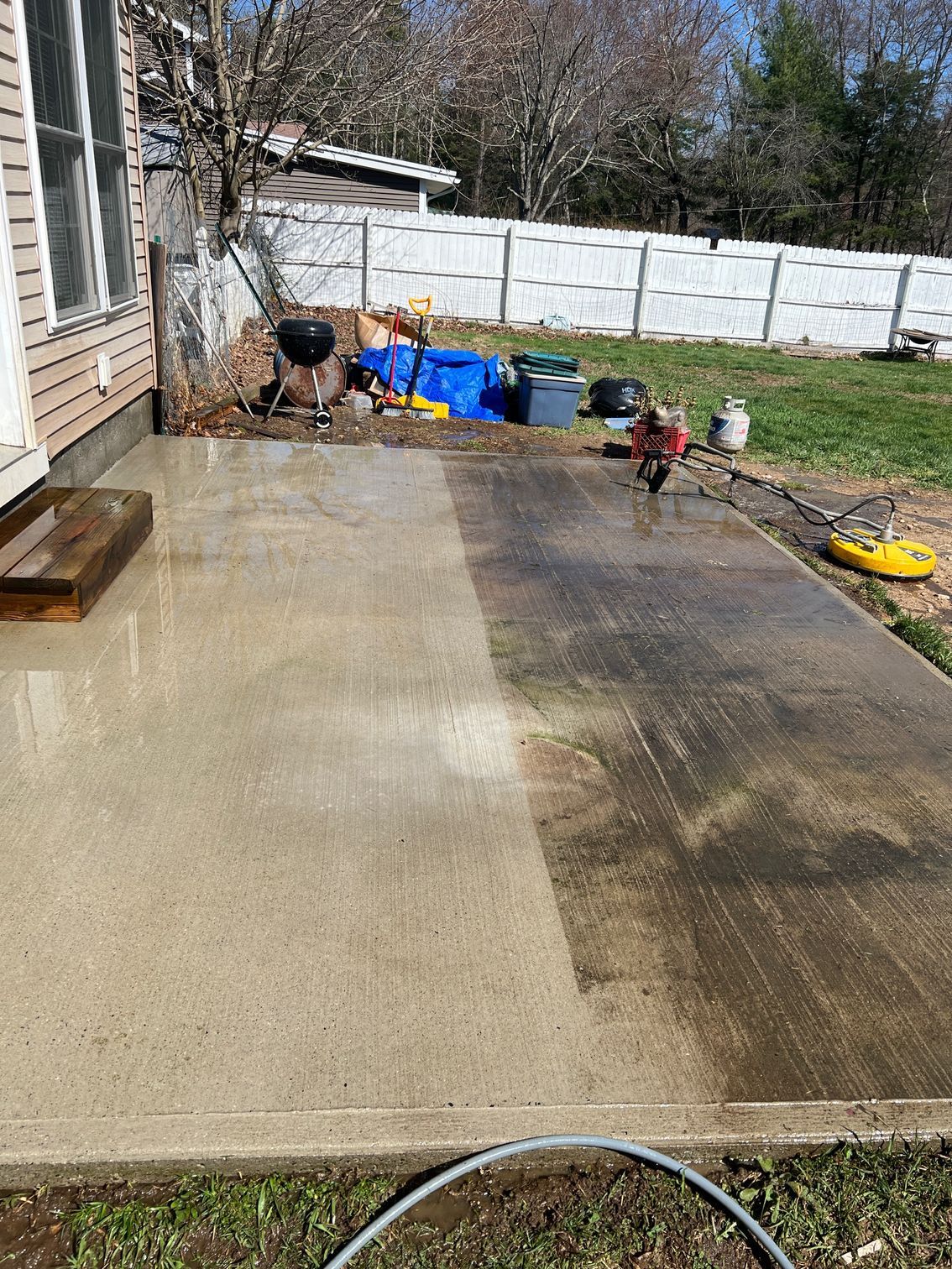 A concrete patio partially cleaned with a pressure washer, showing a stark contrast between the dirty and clean halves.