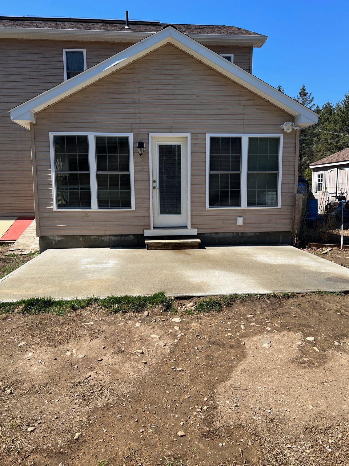 A new light brown siding extension with white trim and a concrete patio.