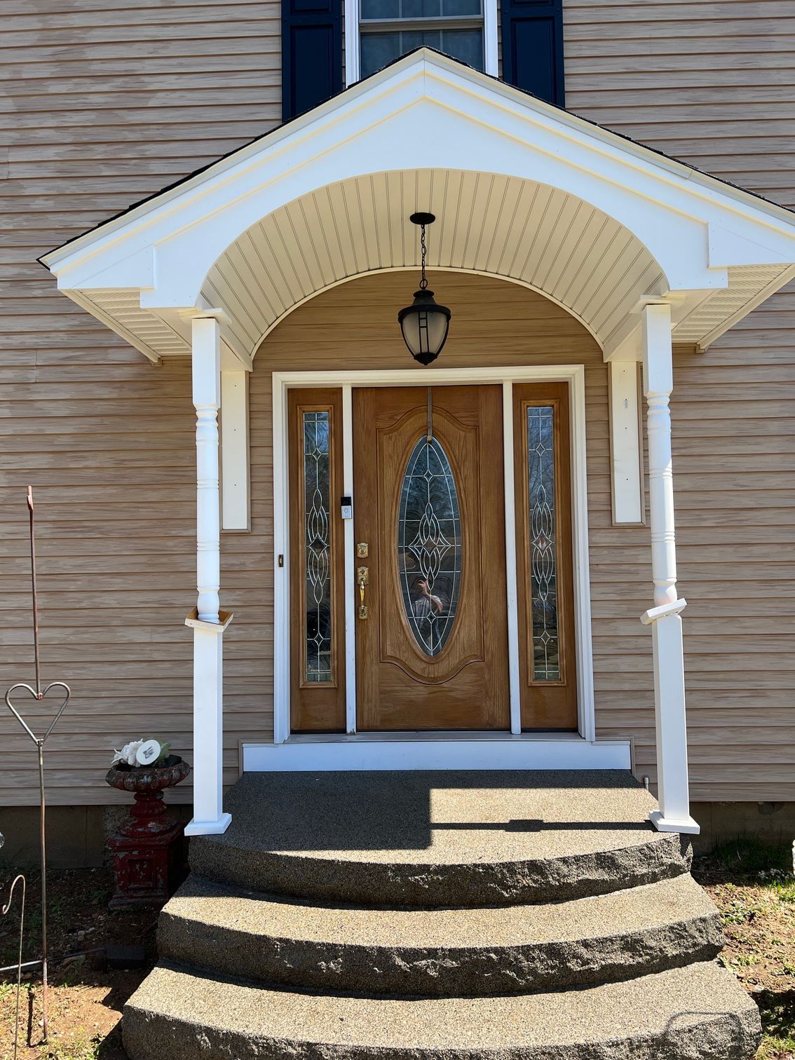 Entrance of a house with a brown wooden door and arched portico supported by white columns. Steps lead up to the door.