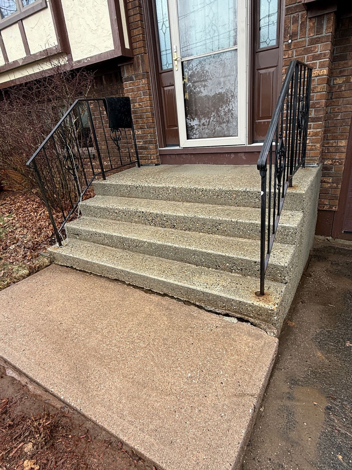 Concrete steps leading up to a brown front door with black wrought iron railings. The steps are a light brown color.