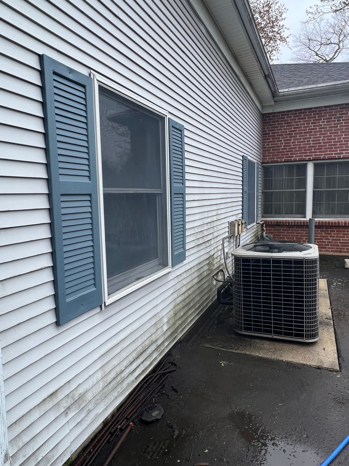 A white house with blue shutters and a black air conditioner on the side.