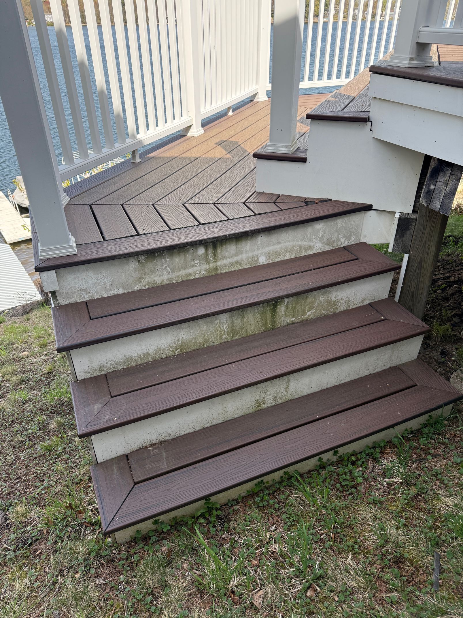 Outdoor staircase with brown steps and concrete risers, leading to a deck with white railing.