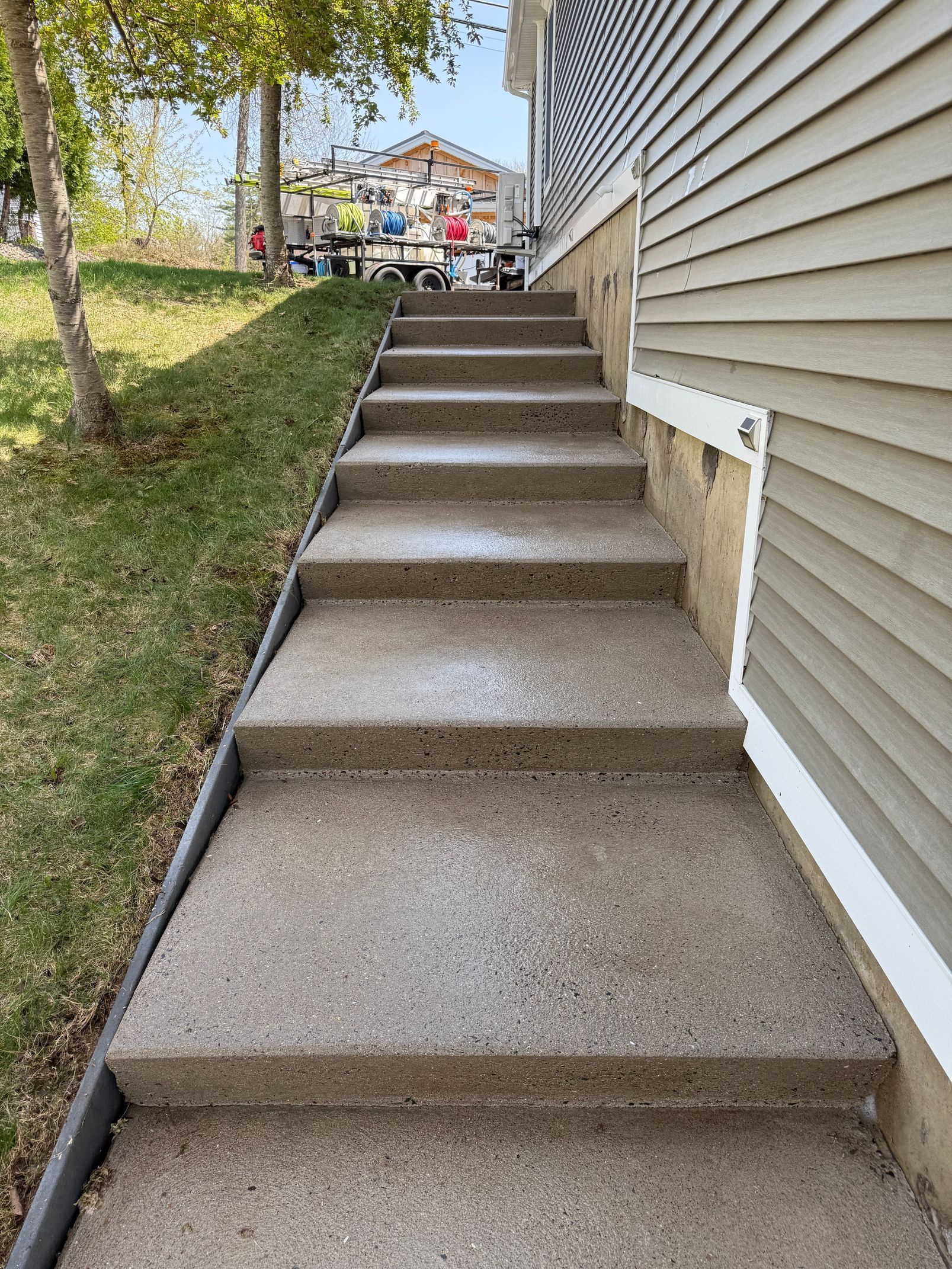 Concrete steps leading up to a building with beige siding. Green grass and a tree are on the left.