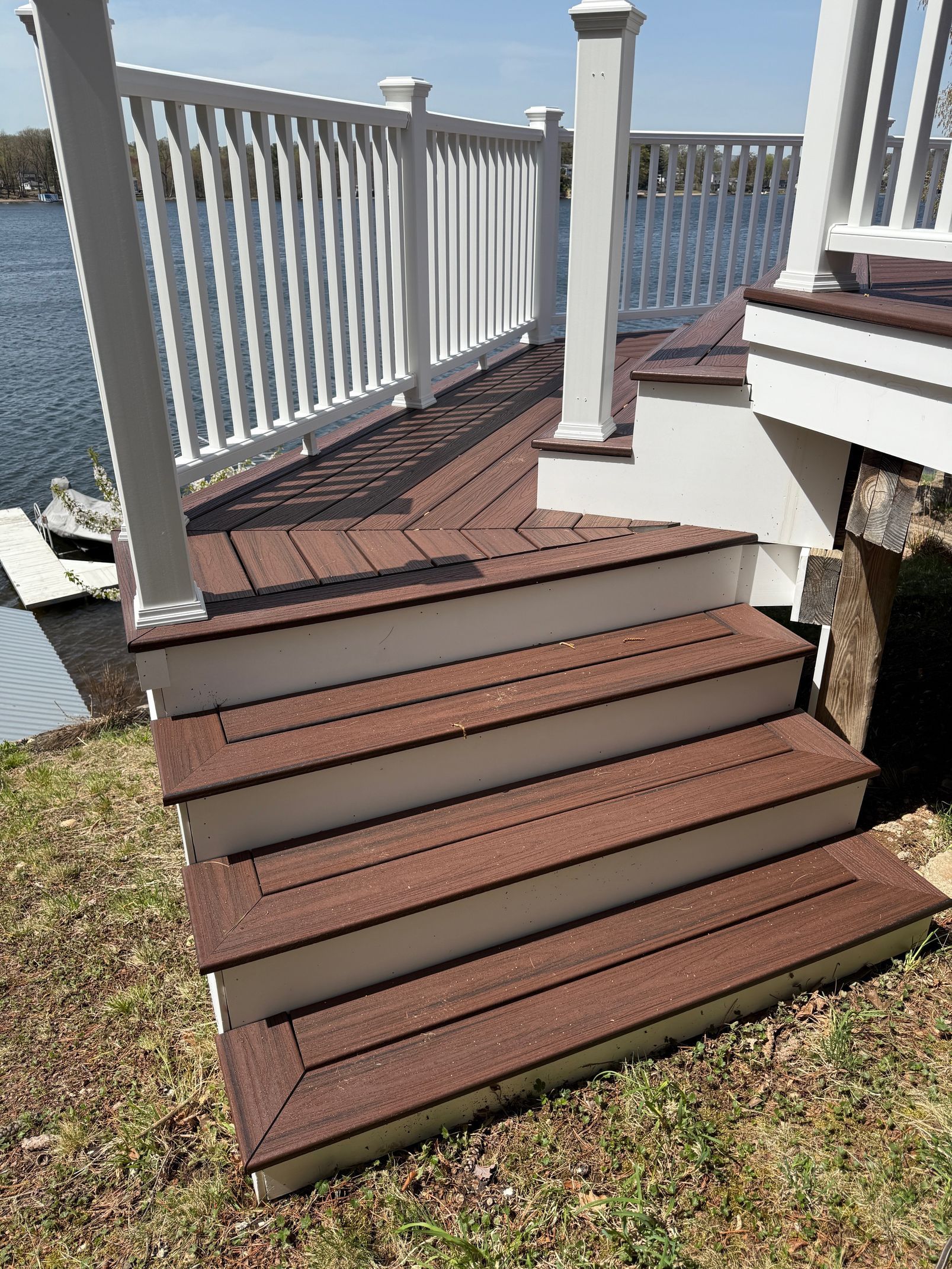 Brown composite deck steps leading up to a white railing and a deck by water.